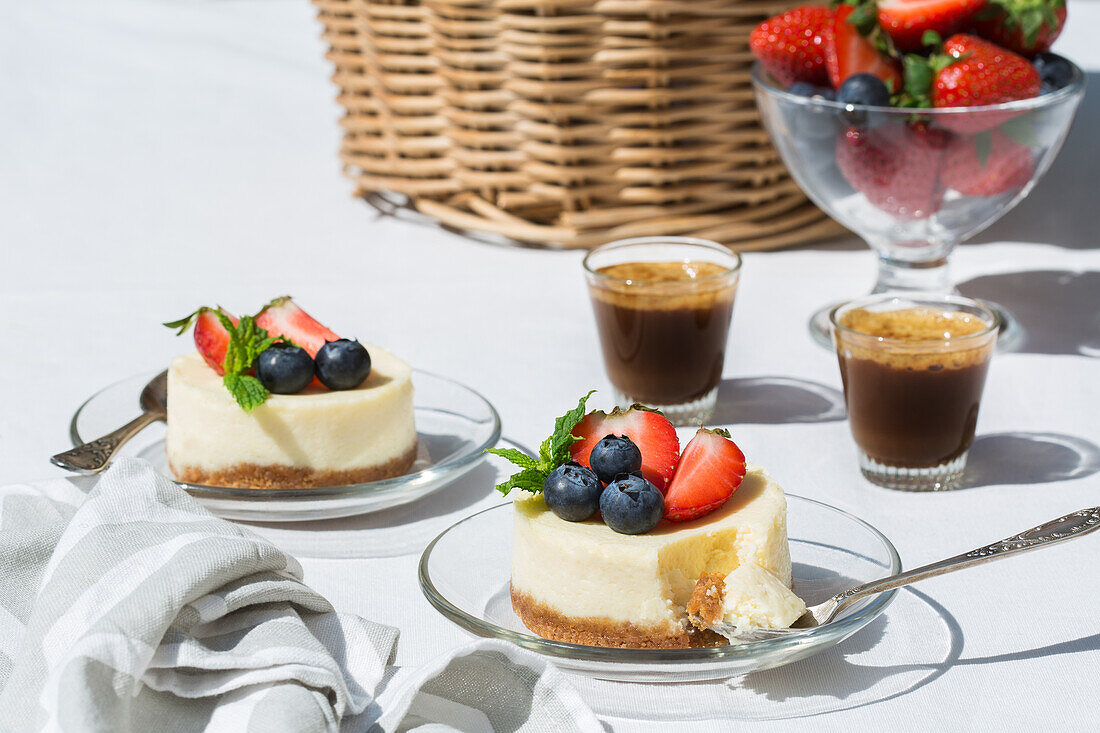 Tasty sweet cheesecakes with blueberries and strawberries served on glass table near cups of coffee