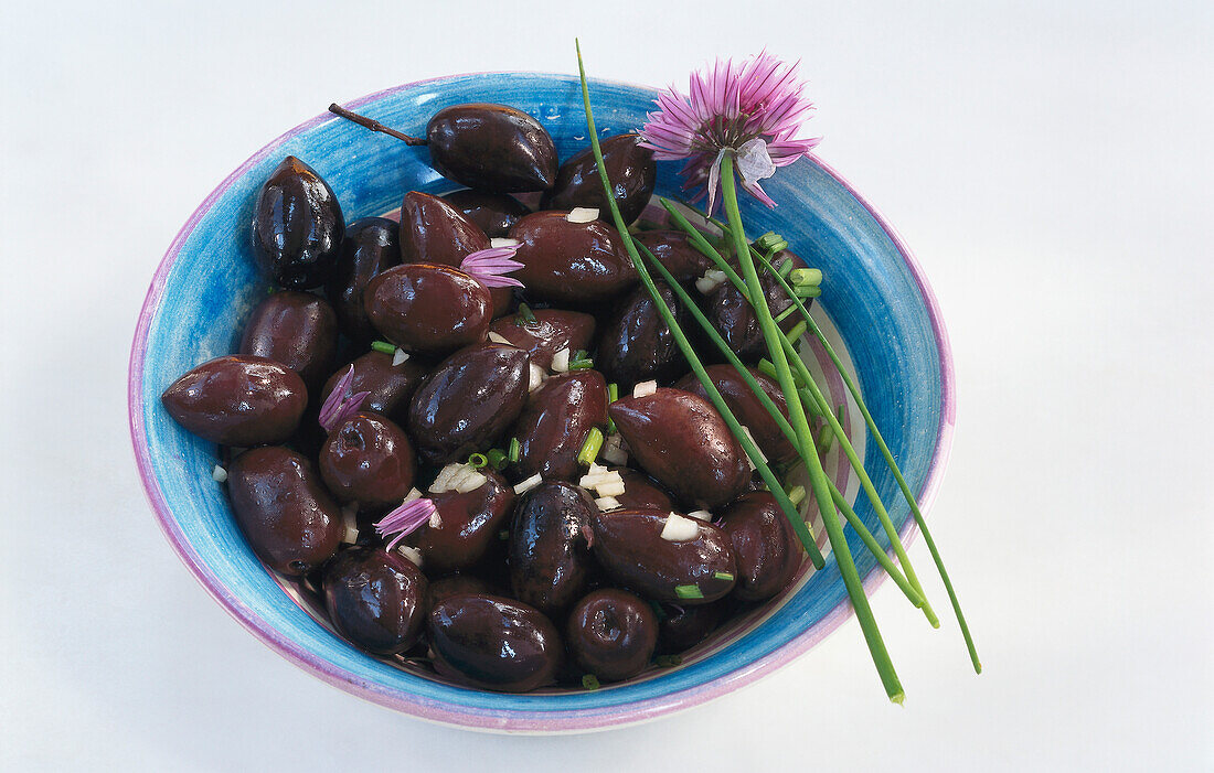 Blaue Schale mit schwarzen Oliven und Schnittlauchblüte