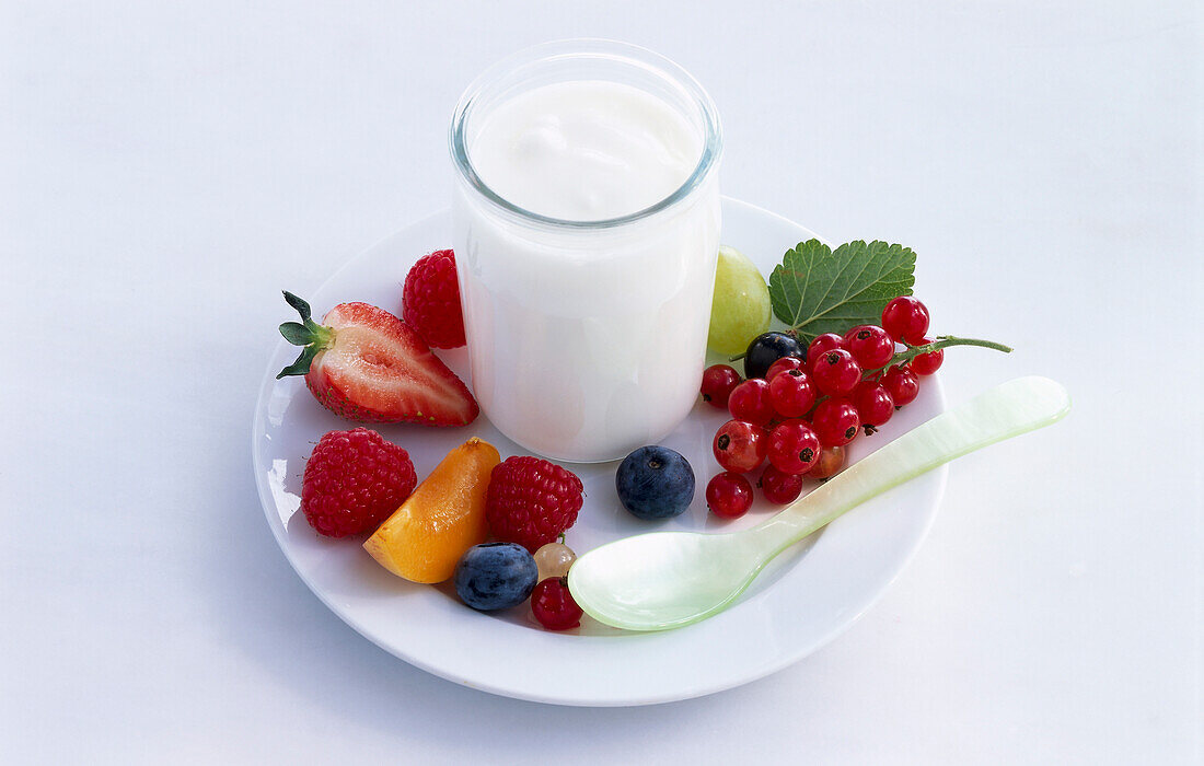 Ein Glas Joghurt umgeben von Obst und Perlmuttlöffel