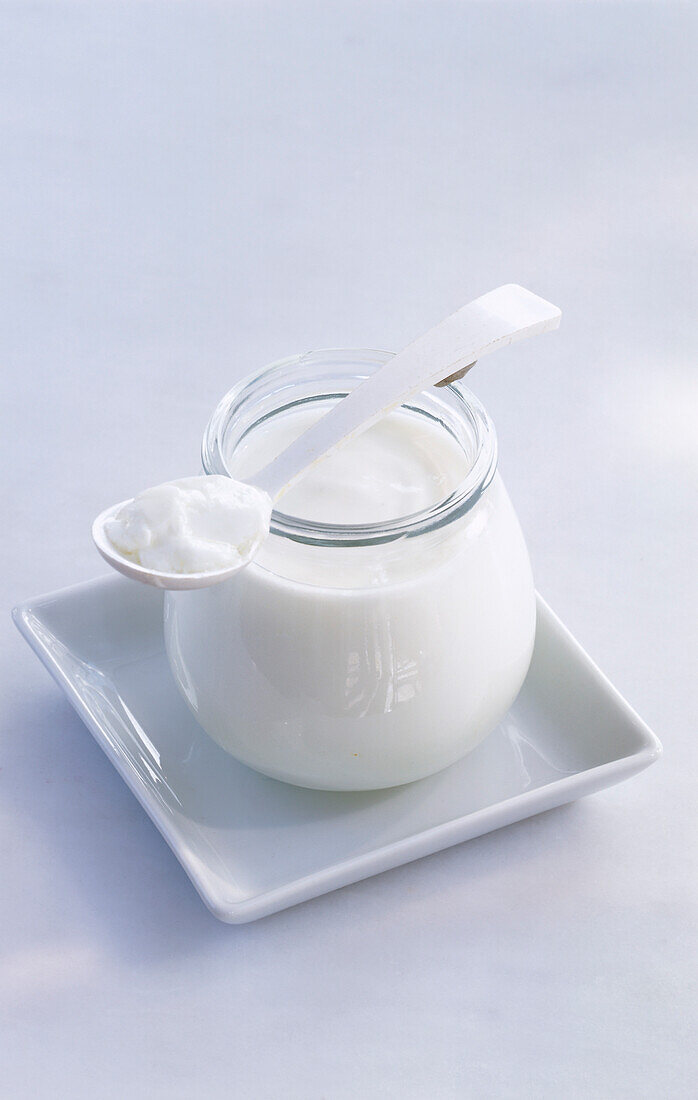 Ein Glas Joghurt mit Löffel auf weißem Schälchen