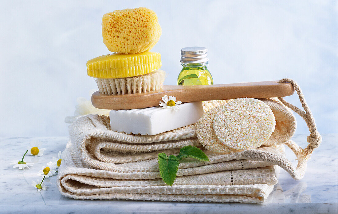 Wellness Stillleben mit Badeschwamm, Loofah, Bürste, Seifen, Handtücher, Kamillenblüten und Duftöl