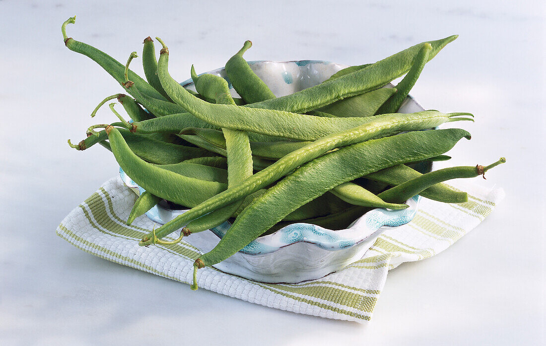 String beans in a bowl, on green and white striped cloth