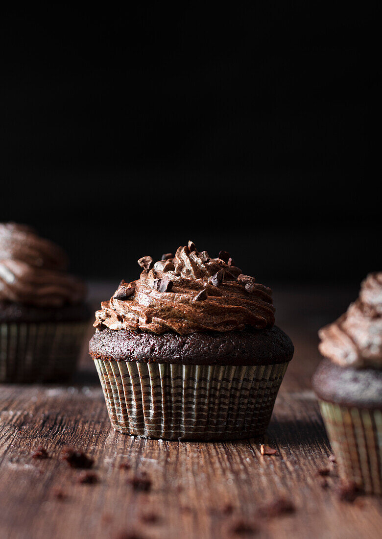 Schokoladen-Cupcakes auf Holztisch vor schwarzem Hintergrund