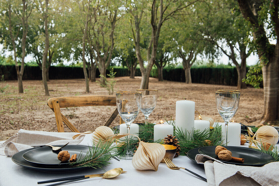 Table setting decorated with candles and cones placed near wooden chairs for Christmas dinner in nature