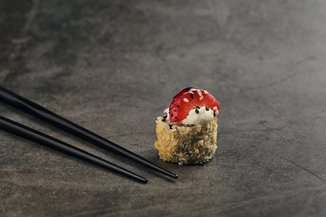 Fried roll of Japanese sushi roll with sesame and strawberry slice near bamboo sticks