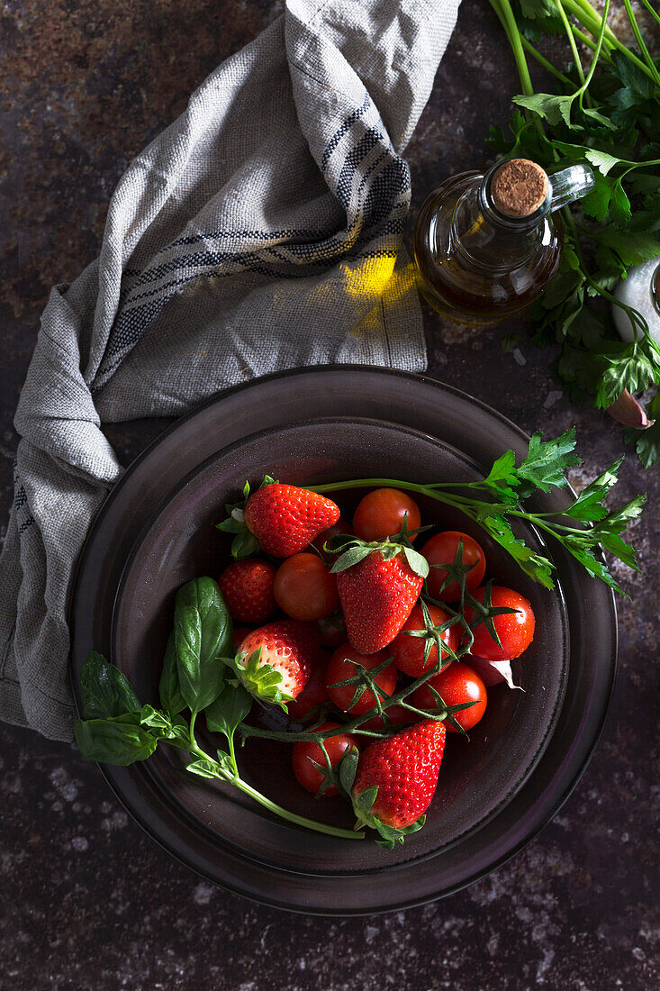 Bowl with fresh strawberry and tomatoes to prepare a gazpacho cold soup placed on dark table