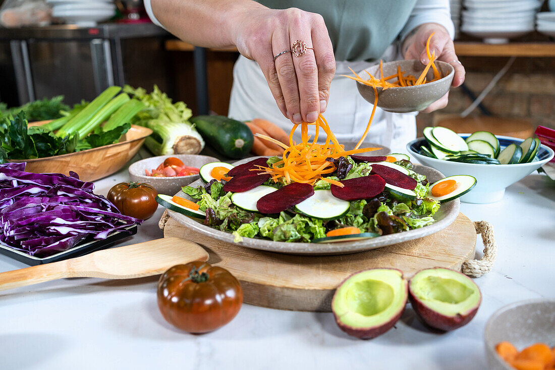 Hände richten Gemüsesalat mit Karottenstreifen an