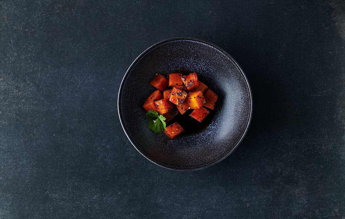 Marinated sweet potato cubes in a black bowl on a dark stone background
