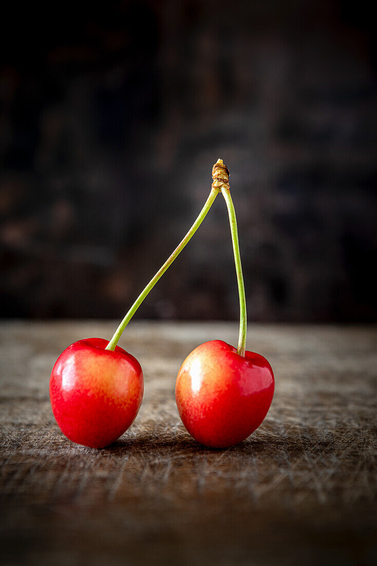 A pair of cherries on a wooden background