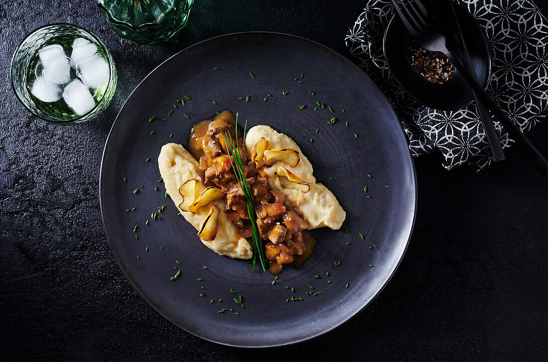 Festive pork goulash with thinly sliced apples on a black plate