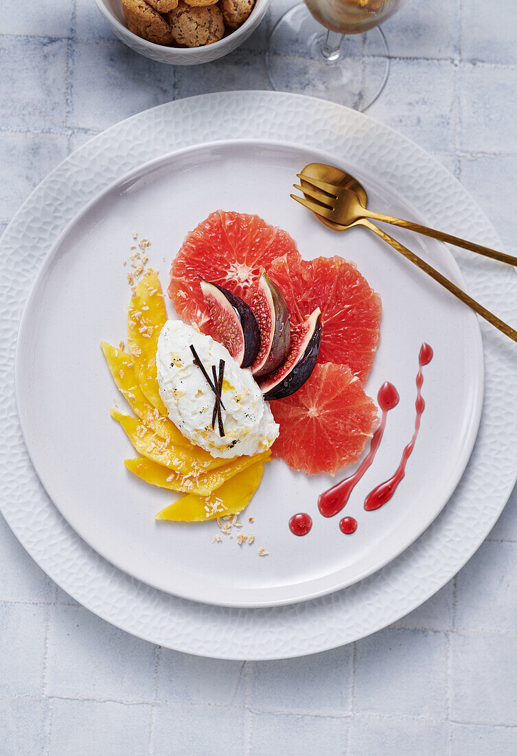 Quark with mango, blood orange, and fig on a white plate with golden cutlery
