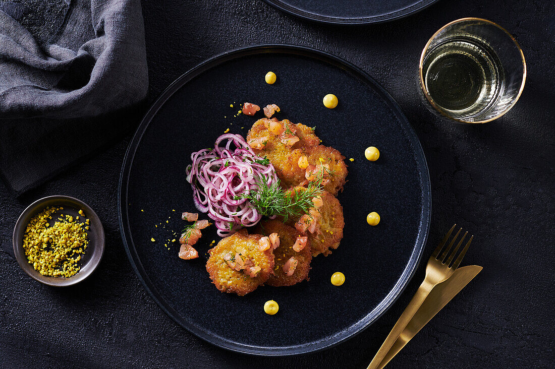 Mini salmon cakes with onion salad on black plate, with golden cutlery