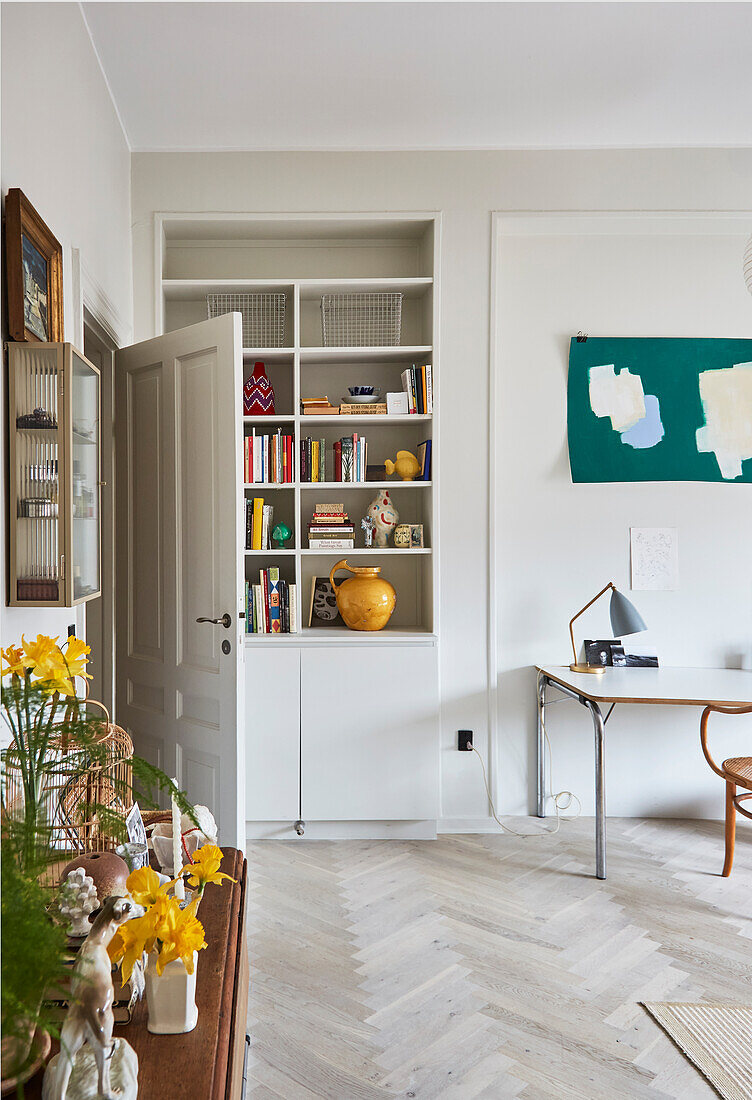 A built-in shelf in a living room with a herringbone parquet floor and a desk