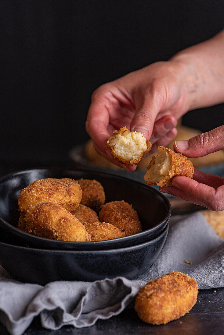 Crop unrecognizable person demonstrating half of yummy deep fried croquette with cheese filling on black background