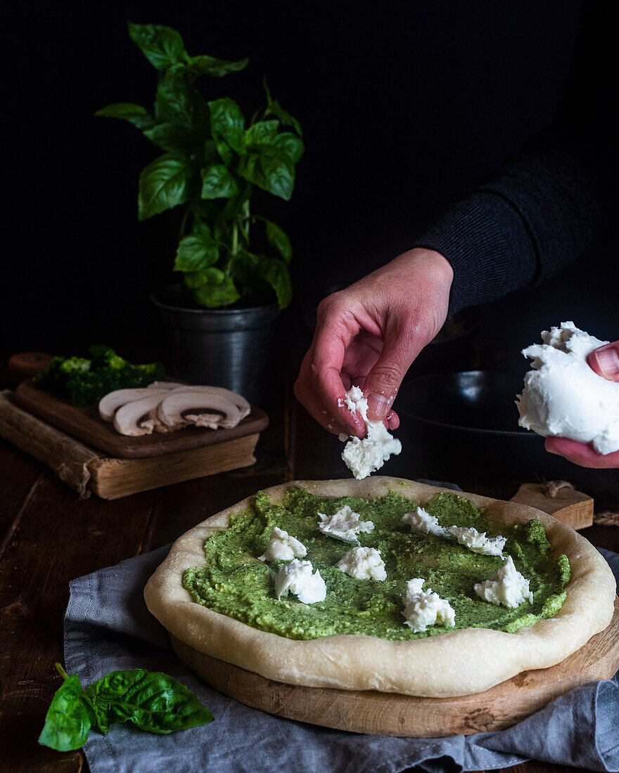 Mozzarella auf ungebackene, vegetarische Pizza mit Pesto verteilen