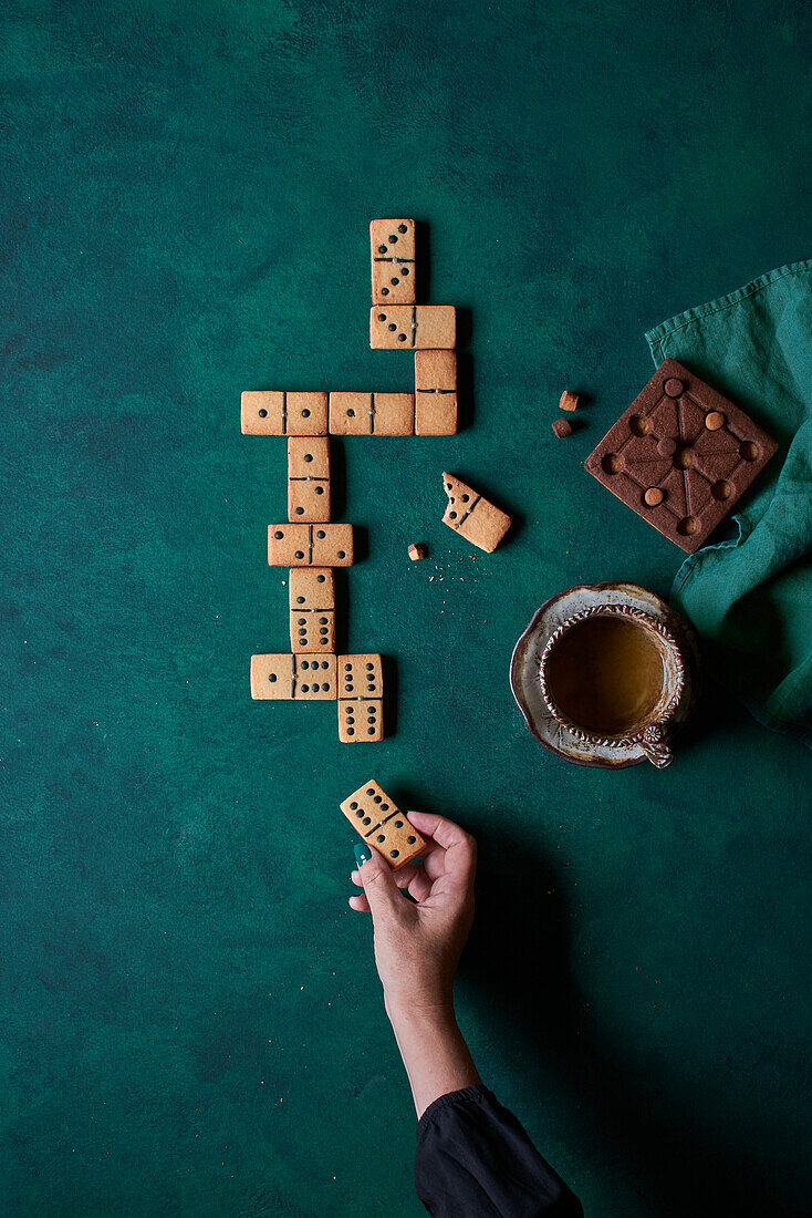 Person eating sweet domino shaped cookies and drinking hot coffee on green background