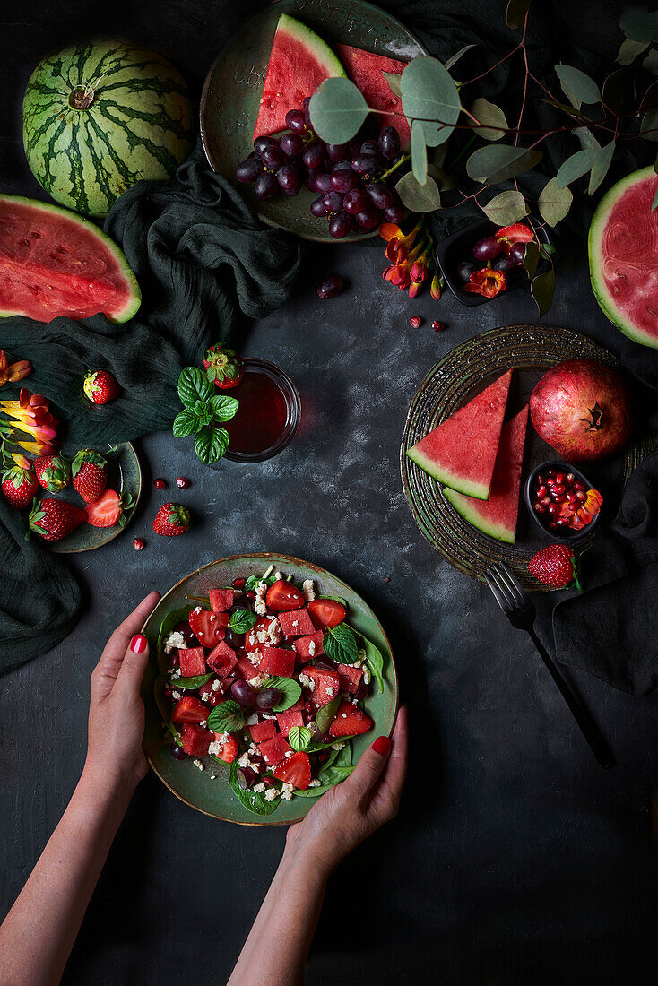 Plate of watermelon salad with strawberries placed on black background with pomegranate and grapes