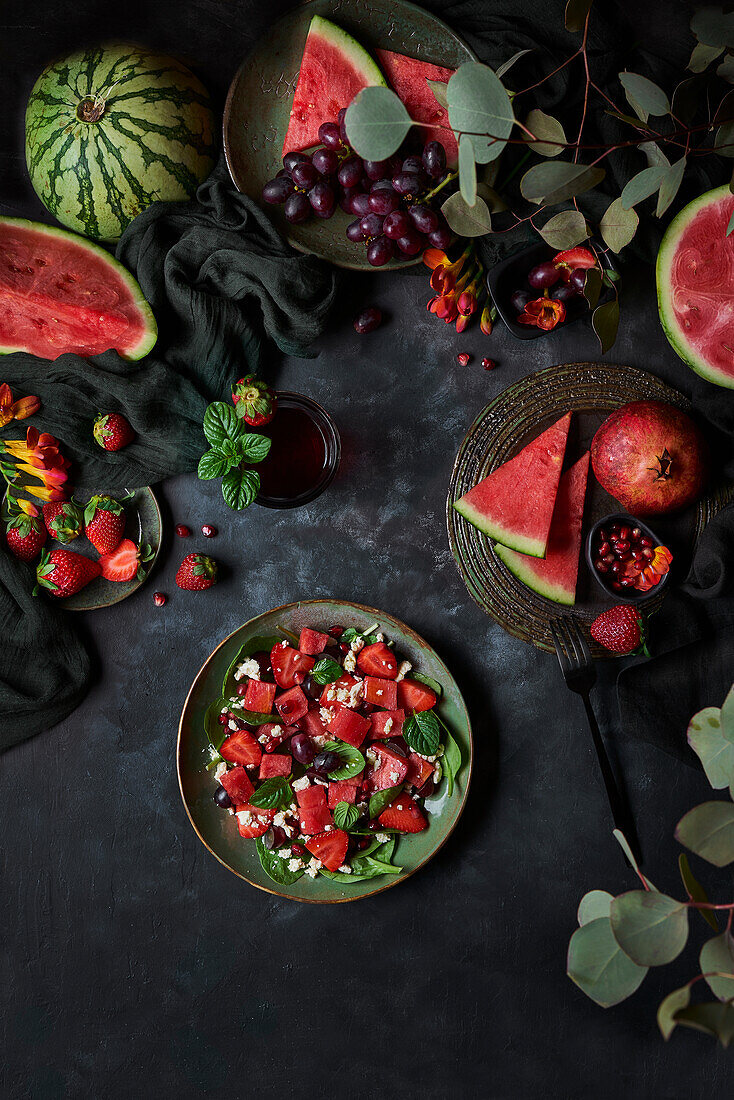 Salad with red watermelon and strawberries placed on black background with ripe pomegranate and grapes