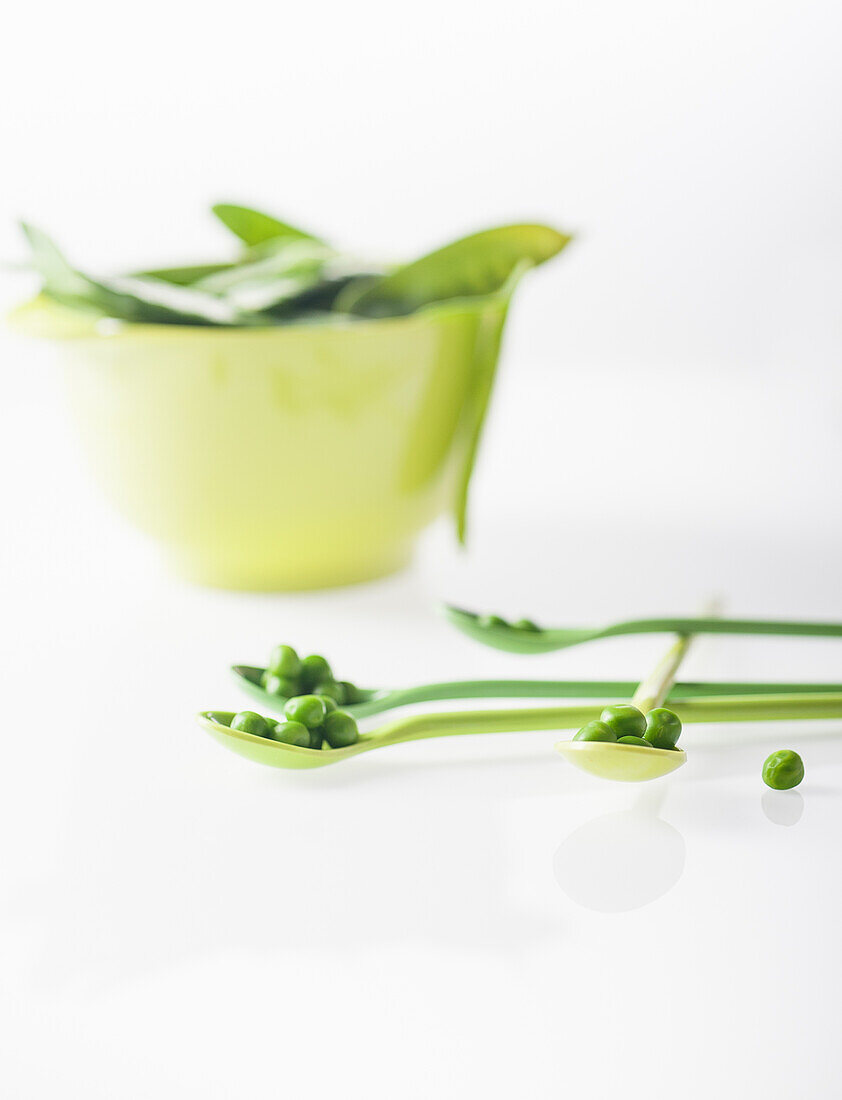 Peas on spoons behind bowl with sugar snap peas