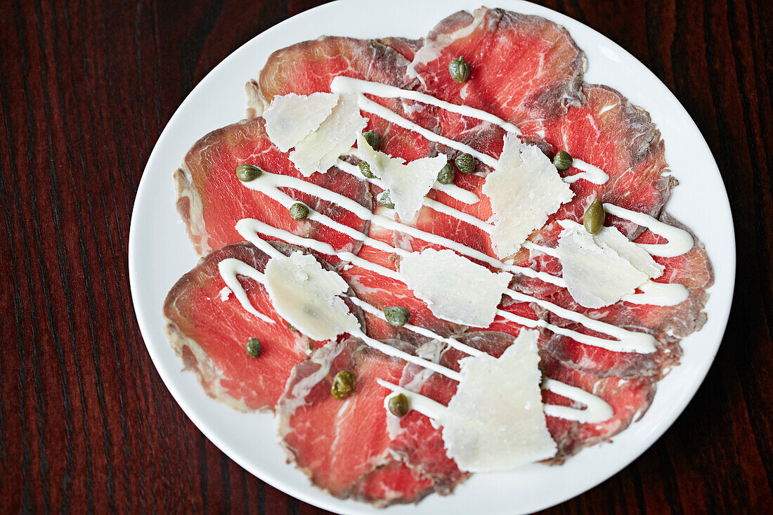 Beautiful bresaola slices on a plate with capers, parmesan and a white sauce