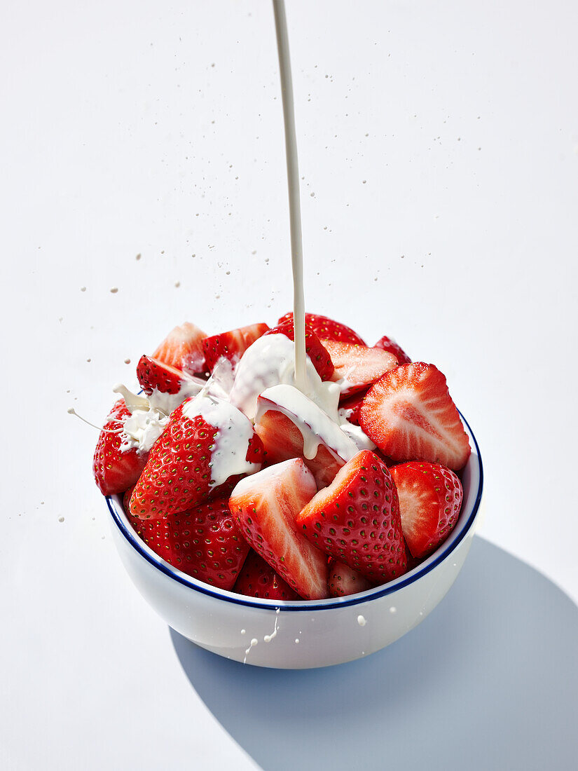 Cream being poured over strawberries in a bowl