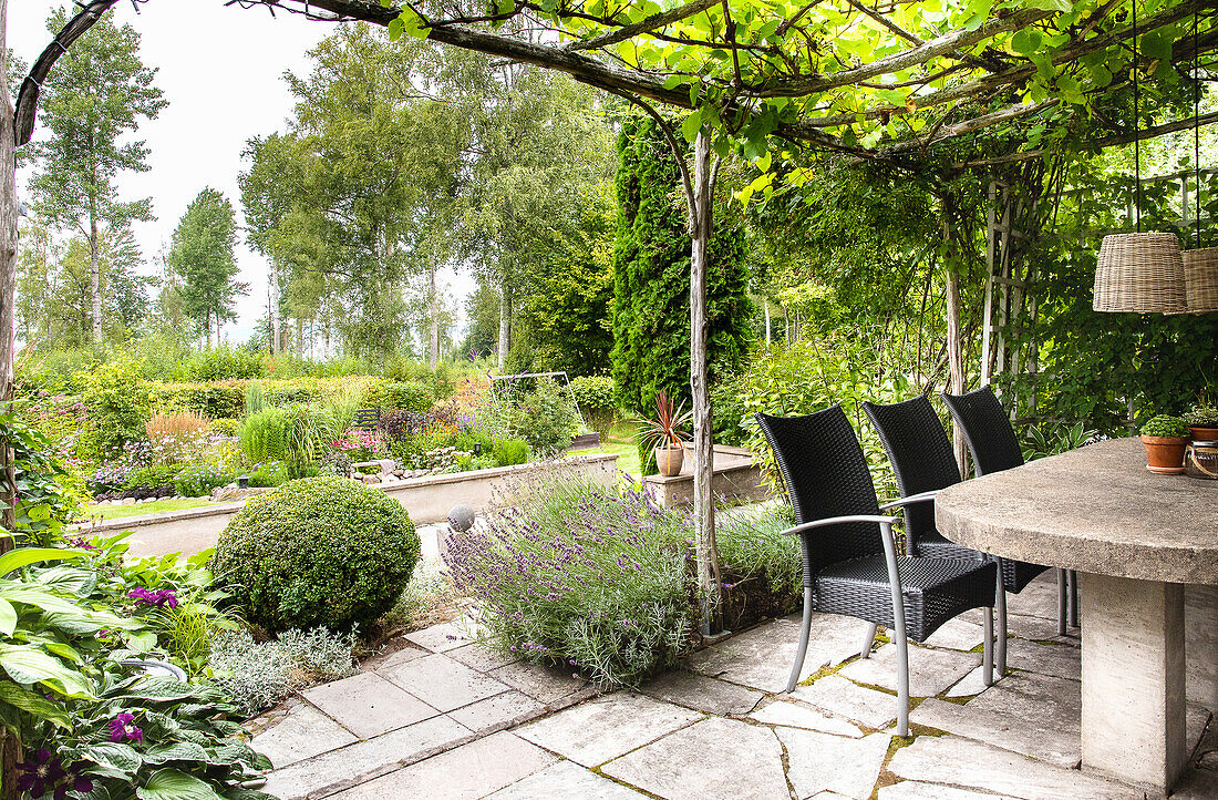 Terrassengestaltung mit Steintisch und Gartenstühlen unter Pergola