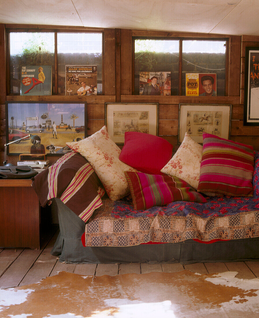 Details a wall of framed images and vinyl records above a traditional sofa displaying a variety of cushions in front of a rug
