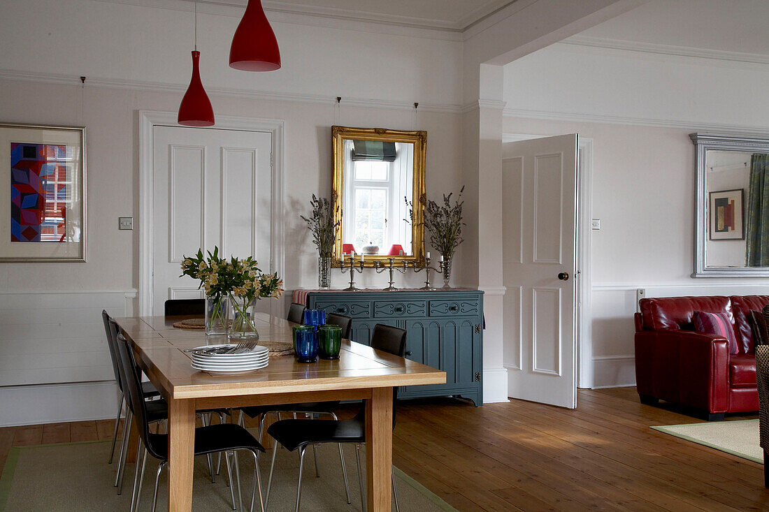 Esstisch aus Holz mit roten Pendelleuchten und bemalter Anrichte in einem Haus in Devon
