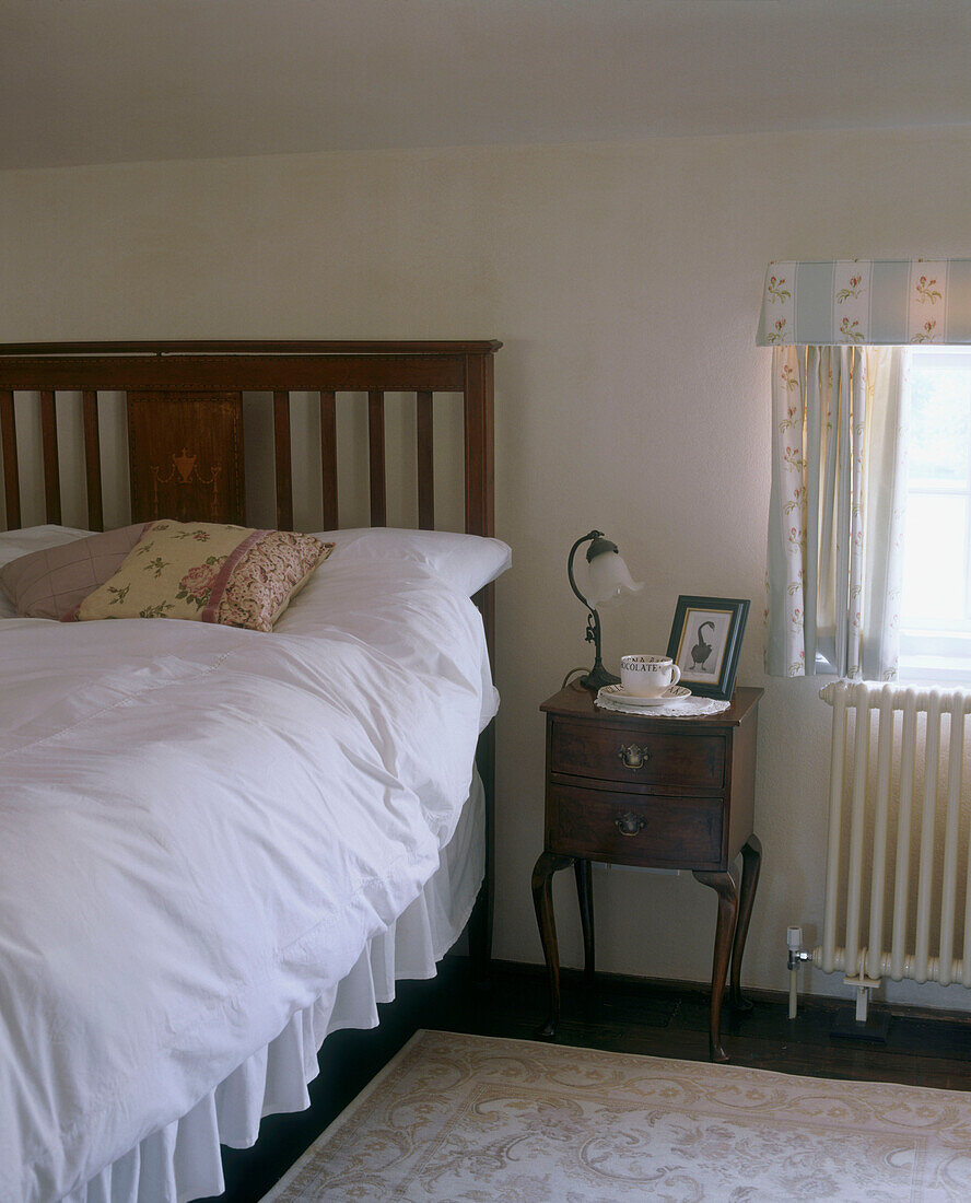 Lamp and cup of tea on a bedside table in a country style bedroom