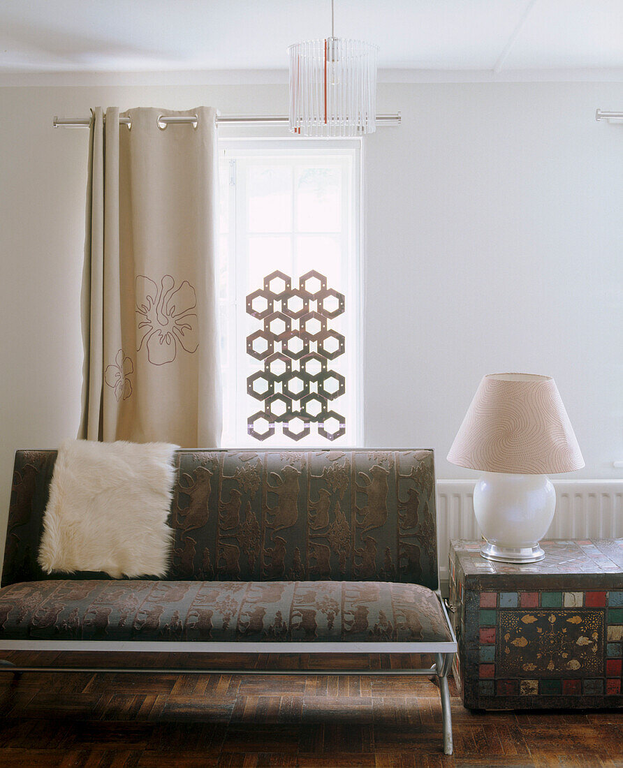 A modern living room with an upholstered sofa window with the silhouette of a contemporary honeycomb mobile hanging down