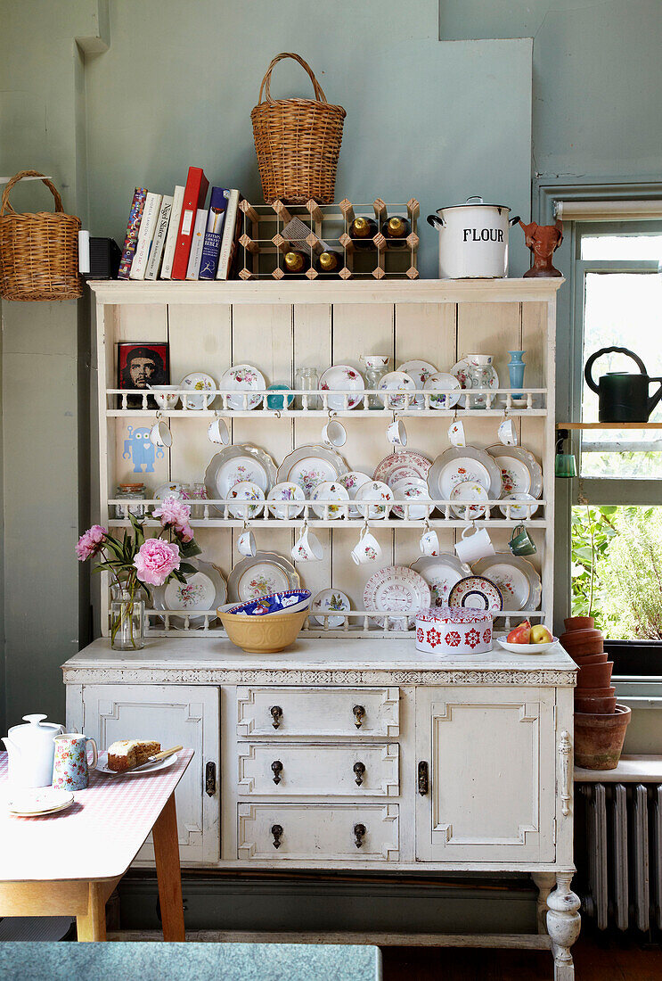 Chinaware stacked in kitchen dresser with recipe books and baskets