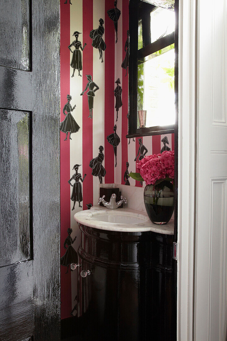 Figurines on pink striped wallpaper with marble wash hand basin in cloakroom of London home
