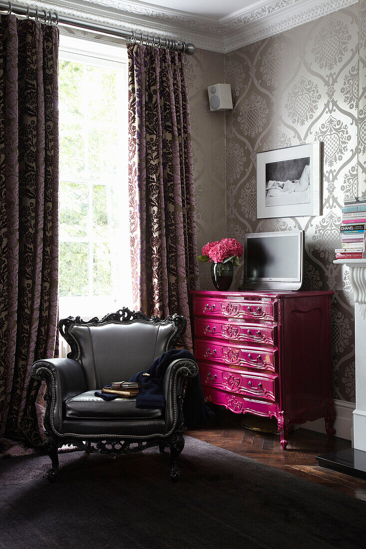 Pink chest of drawers and grey armchair in corner of London fashion designer's home