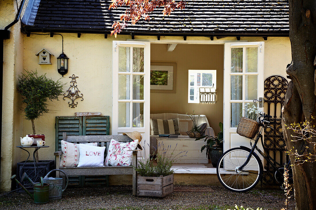 Embroidered cushions on bench seat with bicycle and open door to West Sussex home, England, UK