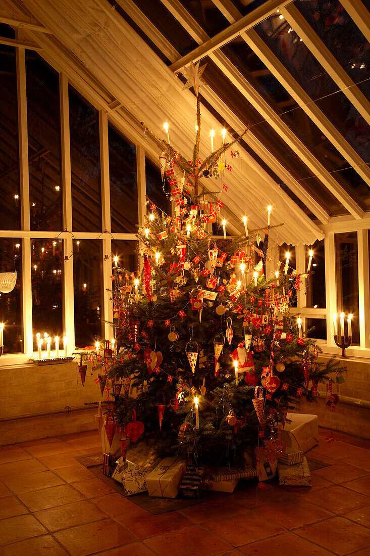 Lit Christmas tree with gift wrapped presents in high-ceilinged conservatory