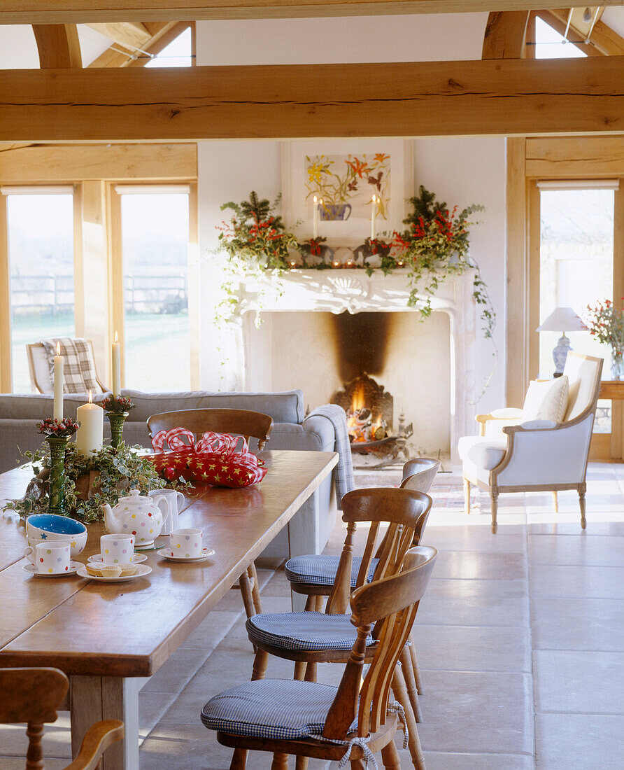 A traditional country dining room with stone fireplace beamed ceiling decorated for Christmas lit fire upholstered armchair wooden table chairs