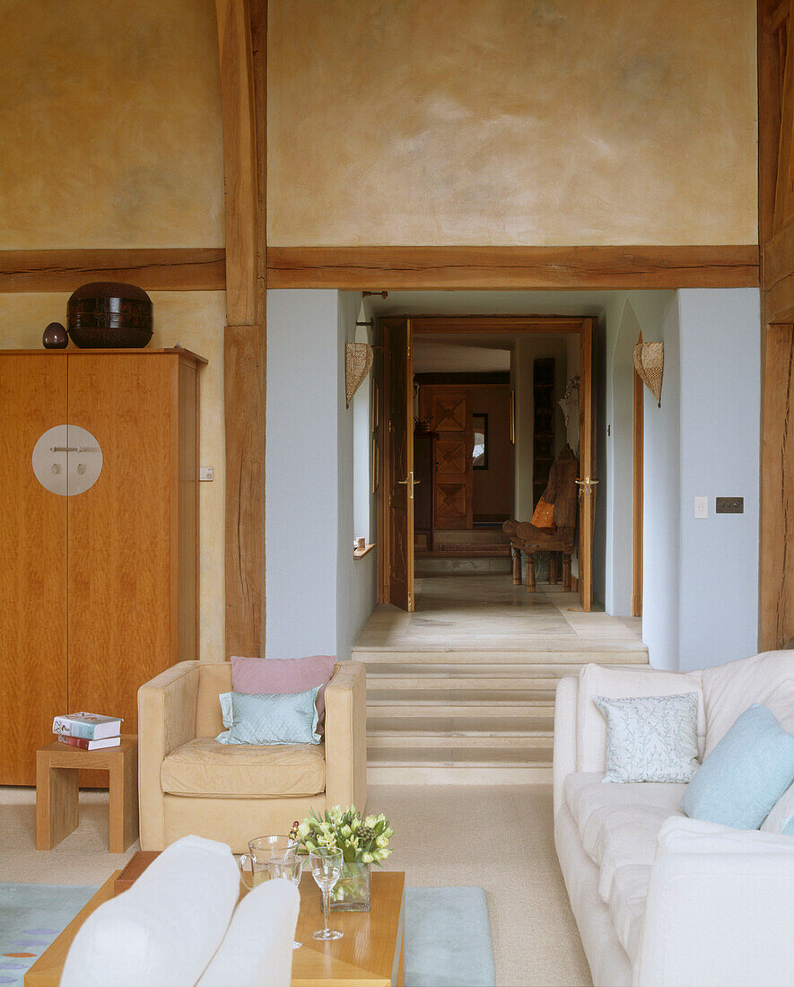 Blick aus Wohnzimmer mit modernem Sofa und Sessel auf eine Steintreppe, die zu einem Flur führt
