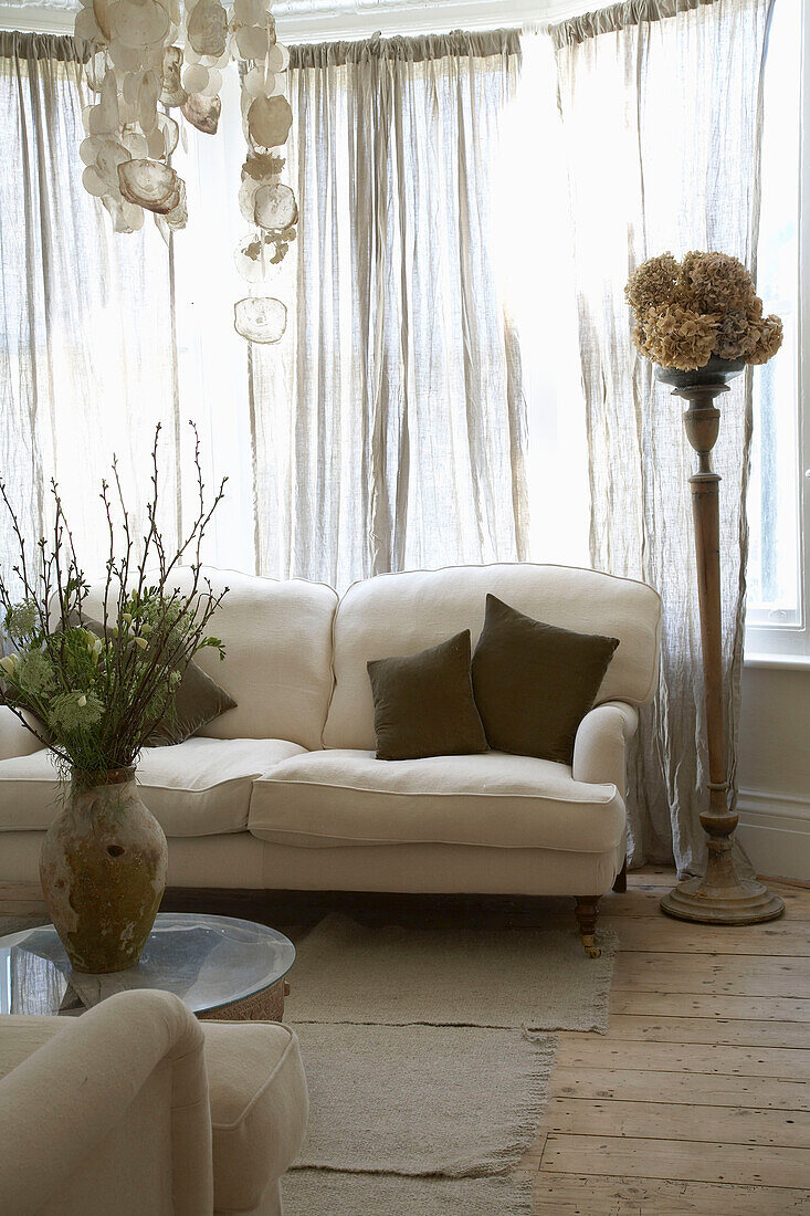 Flower arrangement on coffee table facing sofa in front of window with closed curtain