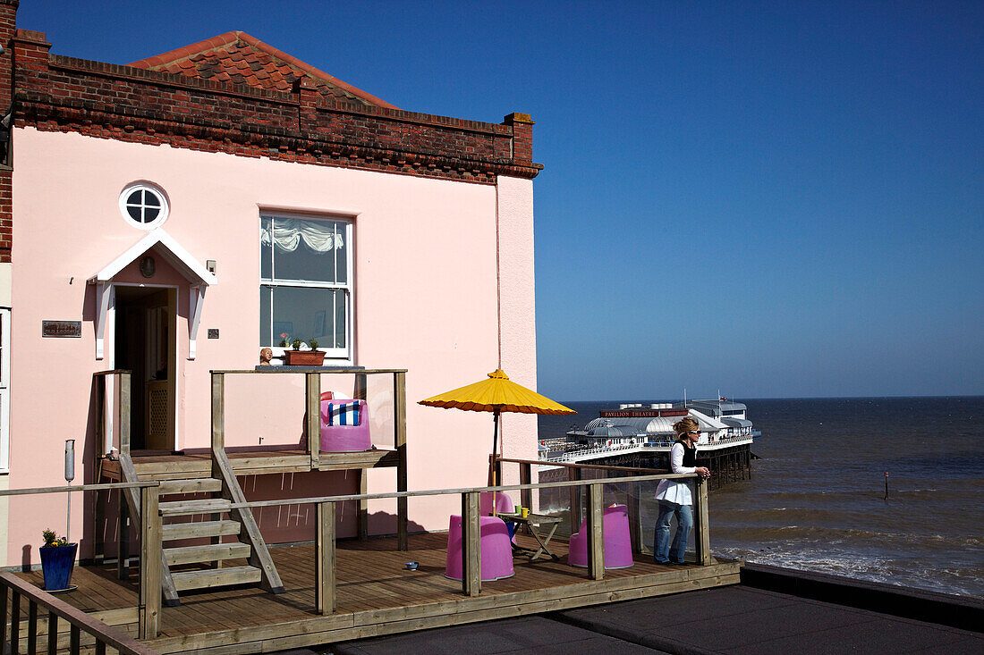 Frau auf der Balkonterrasse eines Strandhauses in Cromer, Norfolk, UK