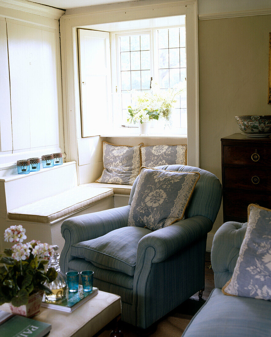 A traditional country cottage sitting room upholstered green armchair pattern cushions window seat
