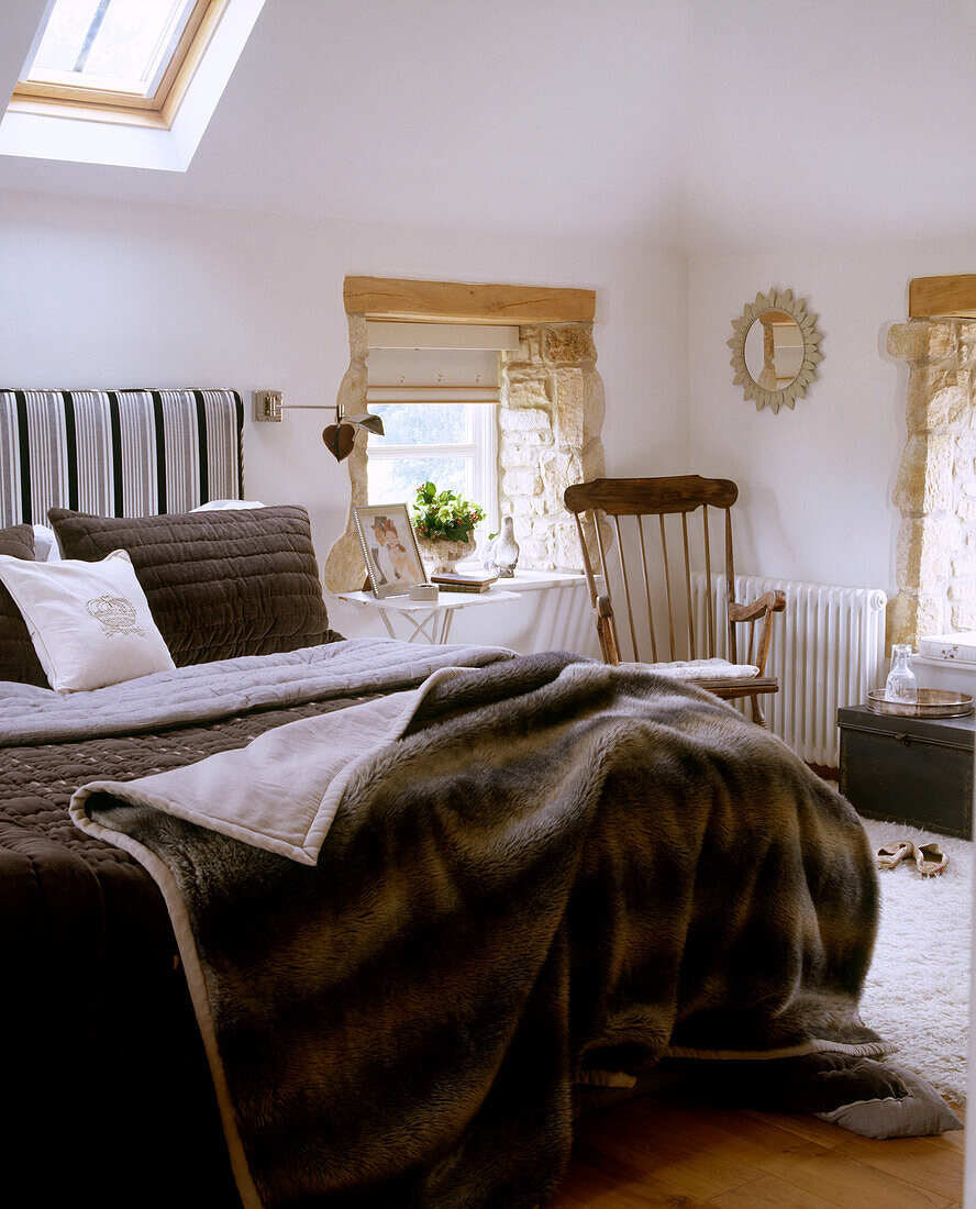 A traditional bedroom with a skylight in a sloped roof above a fur covered bed