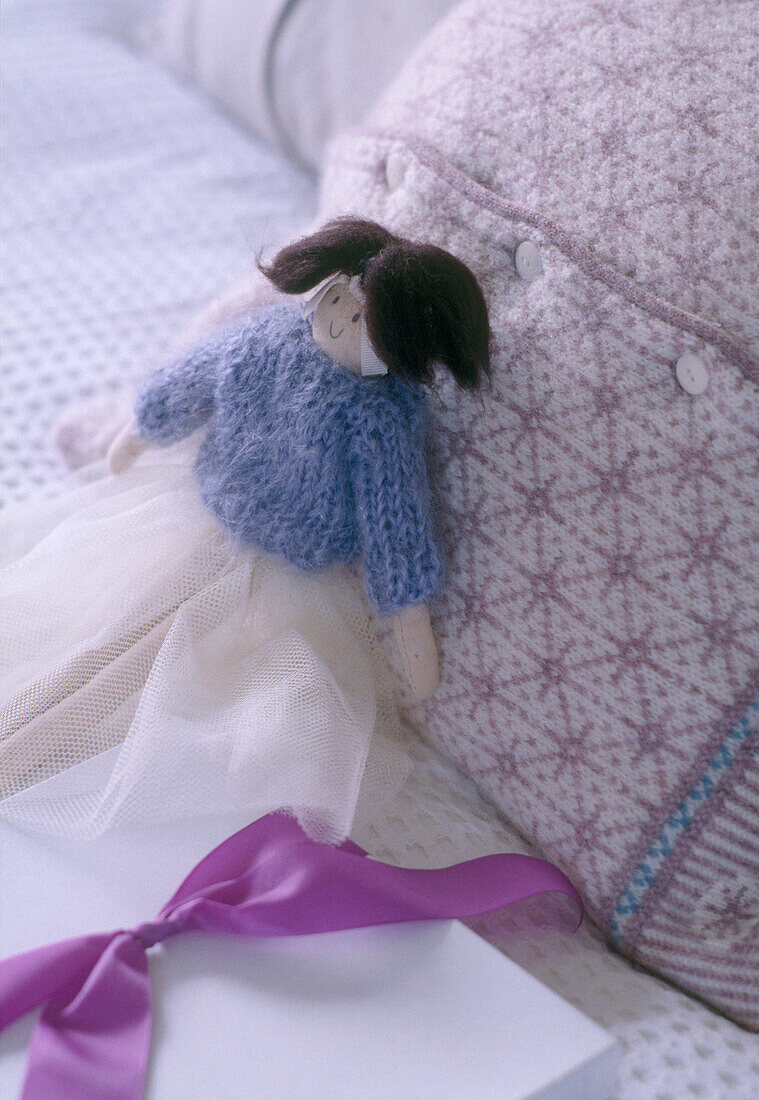 Ein Detail von einem Schlafzimmerbett mit Puppe und einem gestrickten Kissen