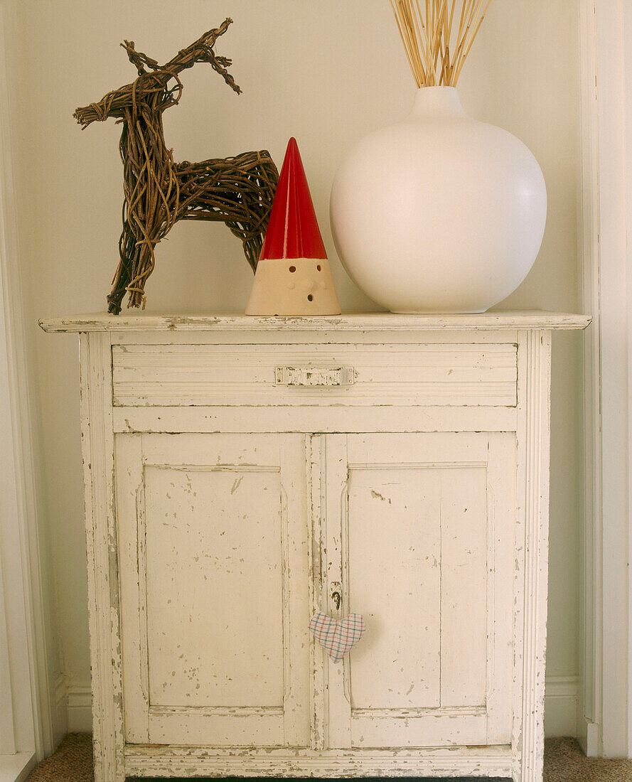 Ein Detail aus einem Schlafzimmer im Landhausstil mit gestrichenem Schrank, Keramikvase, Zweig und Rentierfigur