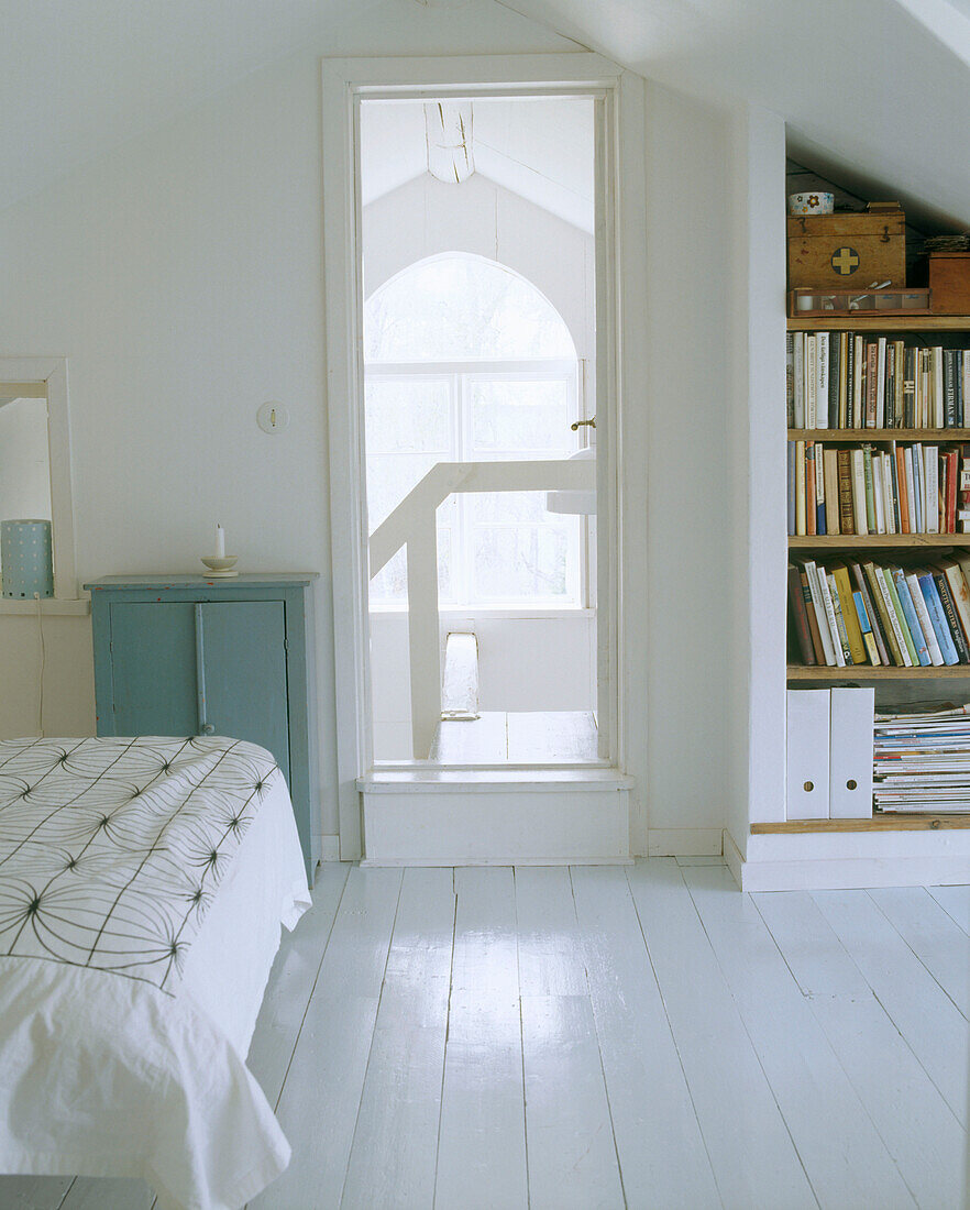 Schlafzimmer mit weiß gestrichenem Fußboden und einem eingebauten Bücherregal hinter der Tür
