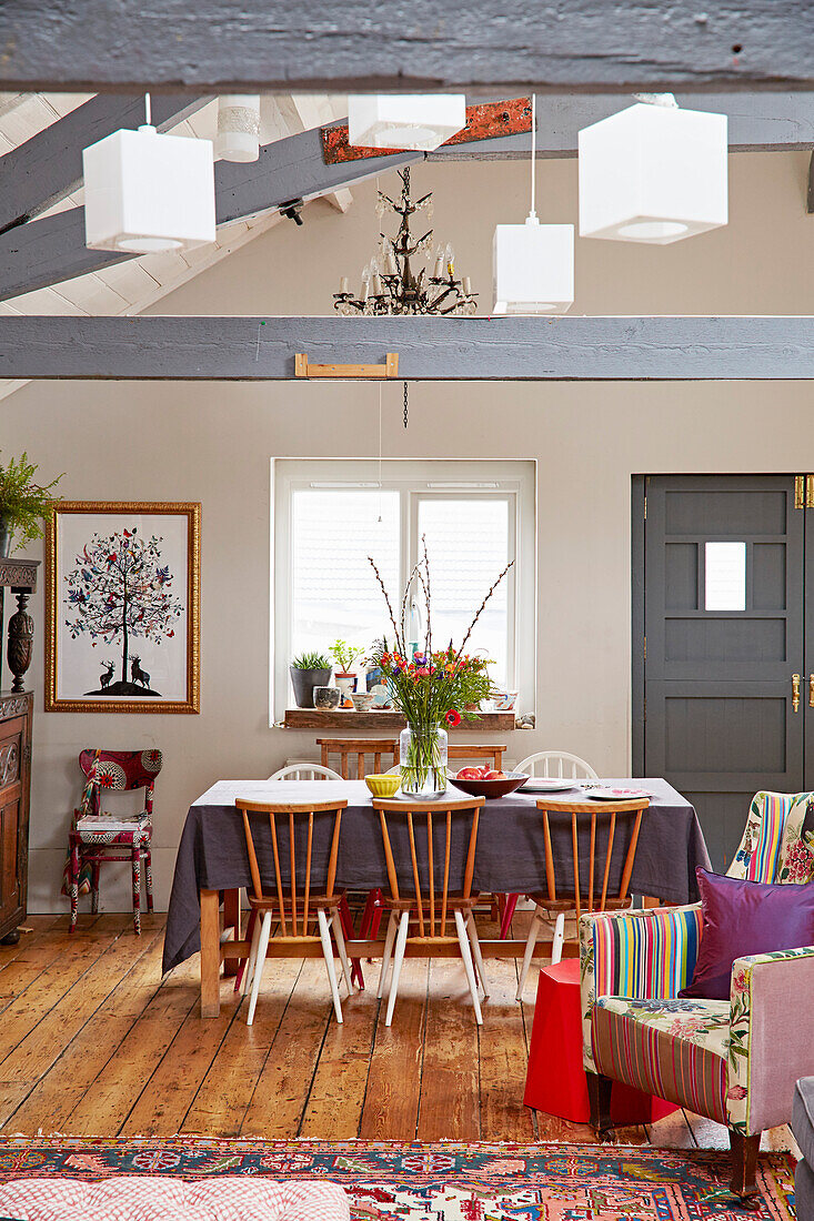 Wooden dining chairs at table with upholstered armchair in Brighton barn conversion East Sussex, UK