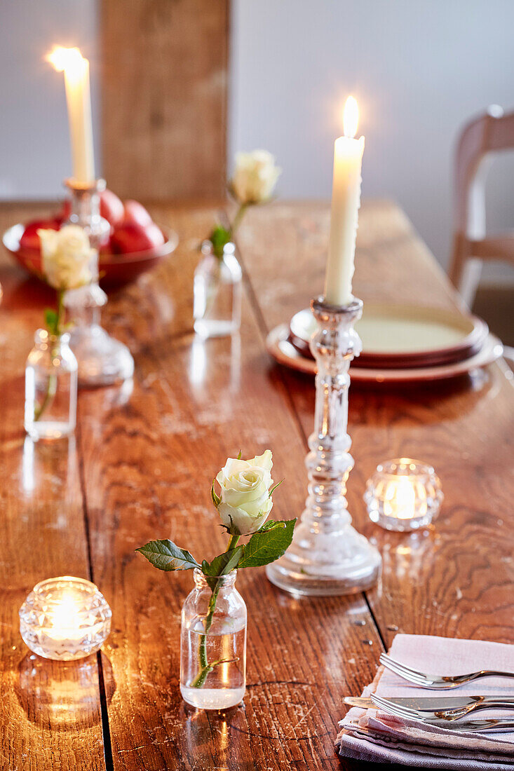 Single stem rose and lit candles on wooden table in Kent farmhouse, UK