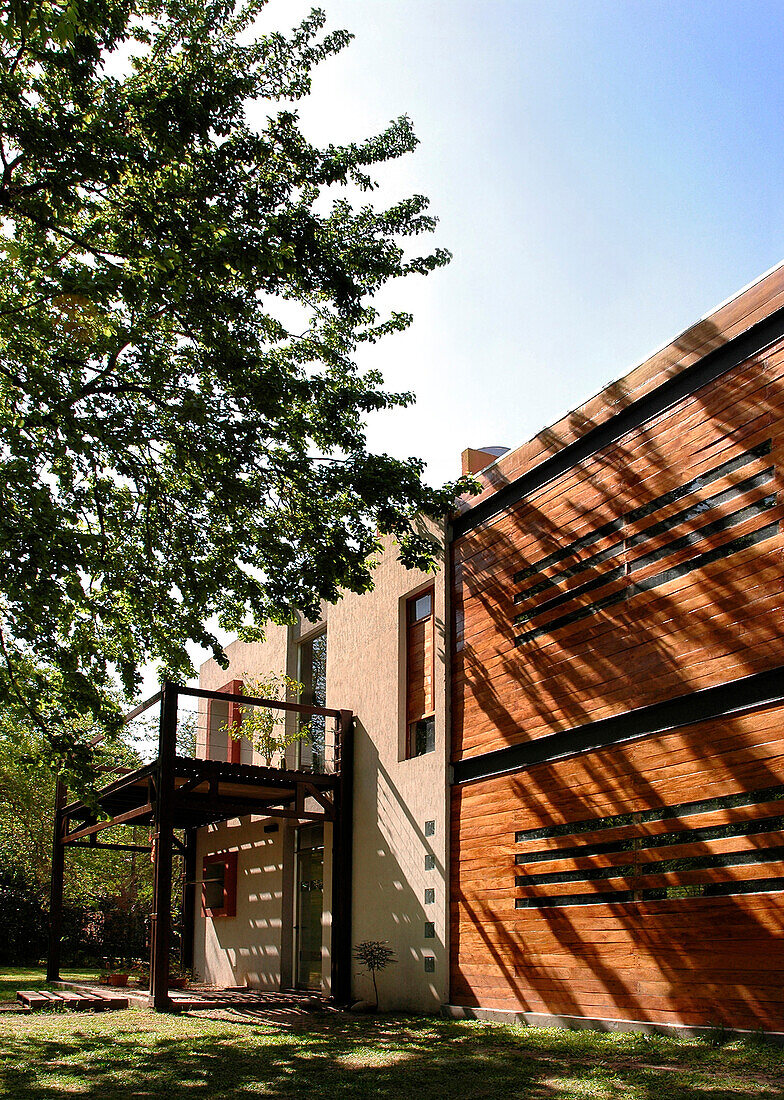 The facade shows a structure made of rusty looking iron which gives shade to the entranceway and becomes a terraced balcony on the upper floor