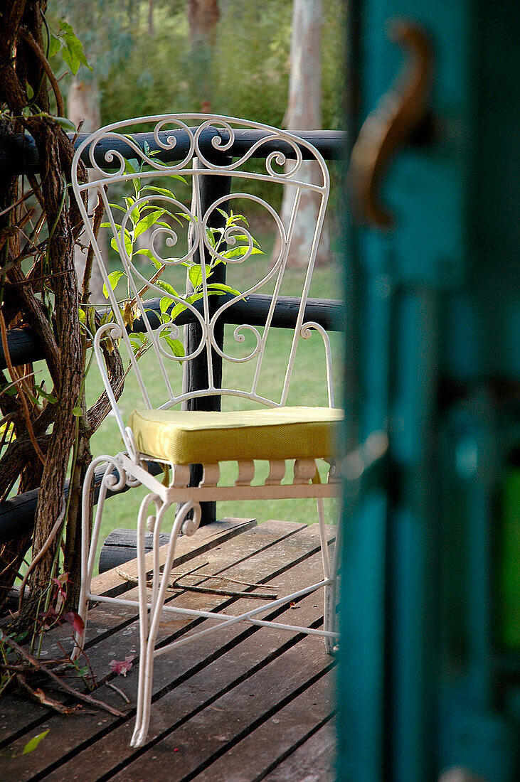 Blick durch Tür auf schmiedeeisernen weiß lackierten Stuhl auf der Gartenterrasse