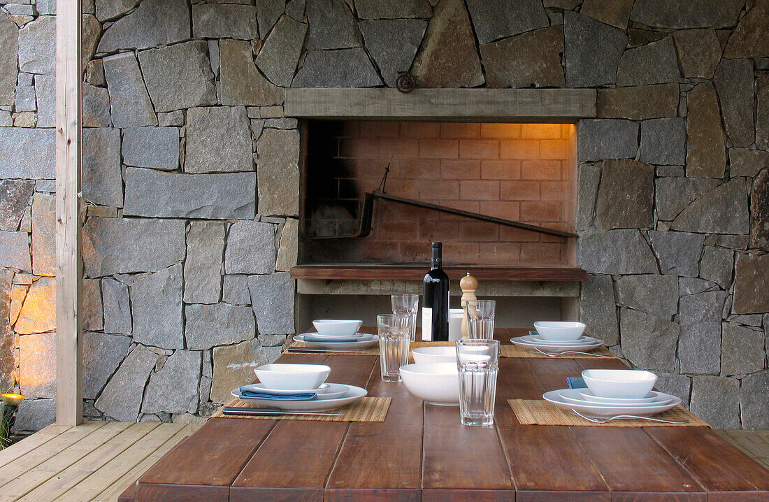 Grill set in exposed stone wall with wooden table and place settings