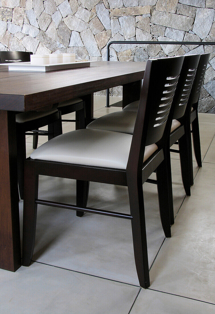 Dark wood chairs set at table on polished cement floor with internal exposed stone wall